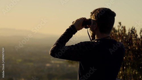 Man standing on a lookout at the top of mountain and watching through binoculars.