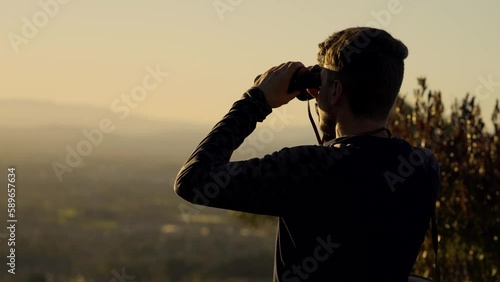 Man standing on a lookout at the top of mountain and watching through binoculars. photo