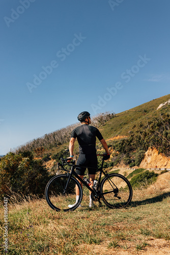 Rear view of a male road bike rider leaning his bicycle while standing in wild terrain