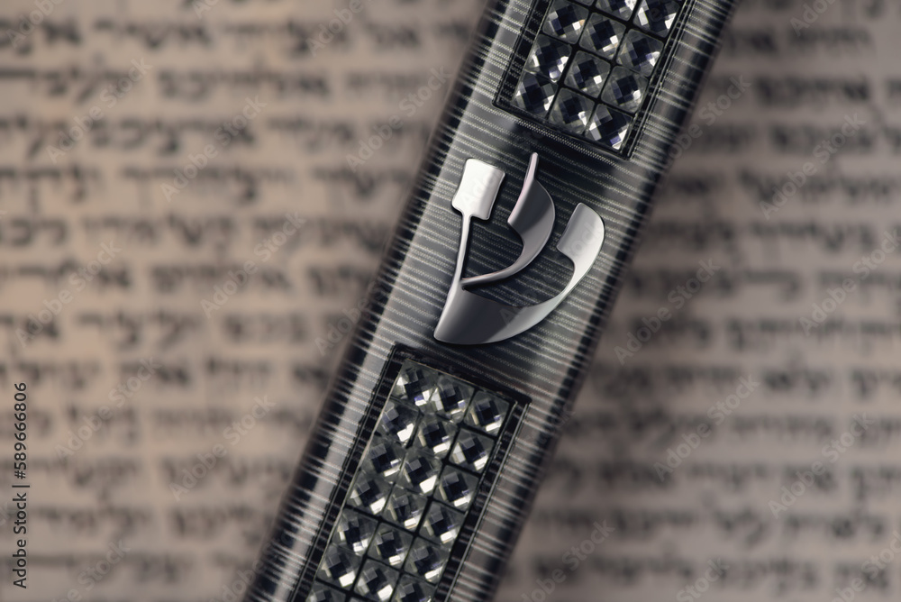 Mezuzah case laying on blurred parchment with Jewish prayer Shema Yisrael in hebrew, mezuzah commandment. Symbol of judaism. Closeup. Selective focus.