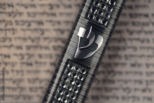 Mezuzah case laying on blurred parchment with Jewish prayer Shema Yisrael in hebrew, mezuzah commandment. Symbol of judaism. Closeup. Selective focus. photo