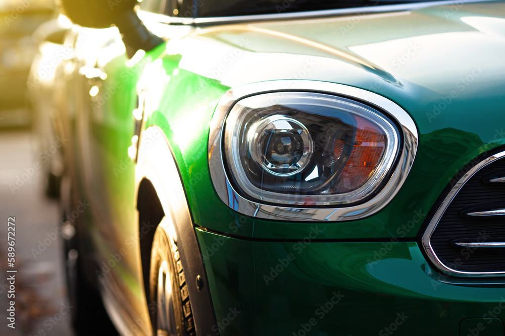 Fototapeta premium Green car, headlight of a modern car close-up with bright sunlight