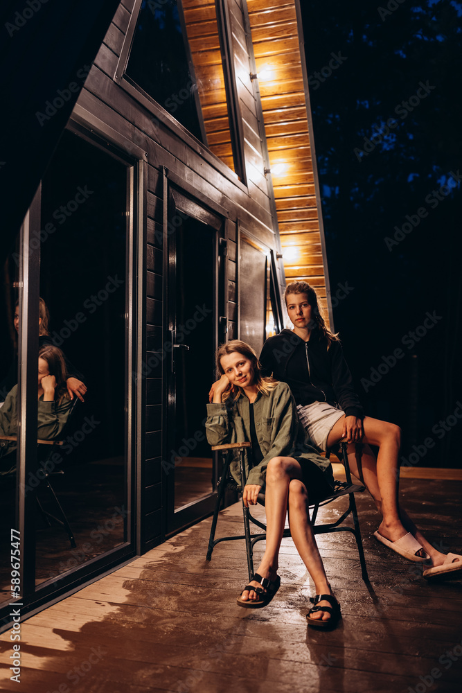 Woman in a country house sitting on terrace and enjoys beautiful view and fresh air. A frame triangle holiday house in the woods at night, peaceful weekend getaway in nature. A frame triangle shape 