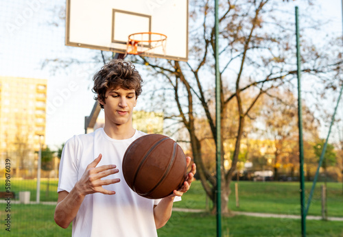 Cute young teenager in t shirt with a ball plays basketball on court. Teenager running in the stadium. Sports, hobby, active lifestyle for boys © Natali