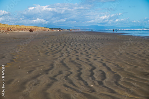 deserted sandy Foxton Beach looking south with sand ripples. In the distance a few people and the Tararua mountains