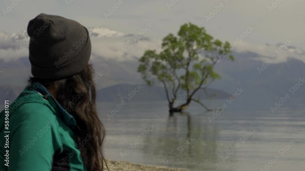 Young woman drinking coffee by the lake with background of Wanaka Tree. Otago, New Zealand Young woman drinking coffee by the lake with background of Wanaka Tree. Otago, New Zealand