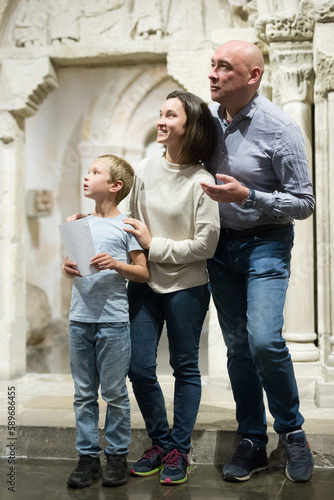 Intelligent man, woman and boy with guide brochure examining exposition in museum hall
