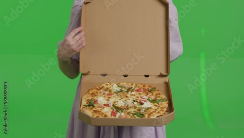 A young attractive red-haired woman holds a box of thin Italian pizza. Smiling girl in a linen dress on a green background photo