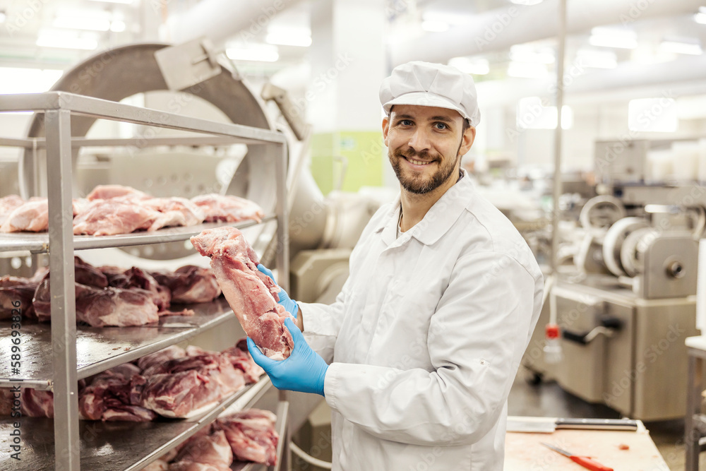 A meat factory worker is holding piece of raw meat and smiling at the camera. A meat factory worker is holding piece of raw meat and smiling at the camera.