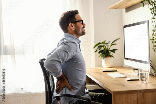 A remote worker is having back pain while sitting at his home office. photo