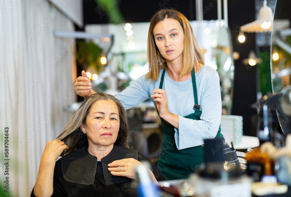 Professional hair stylist discussing elderly female customer preferences in salon, choosing new hairdo.