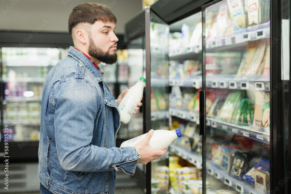positive bearded man shopping for milk products at supermarket food department