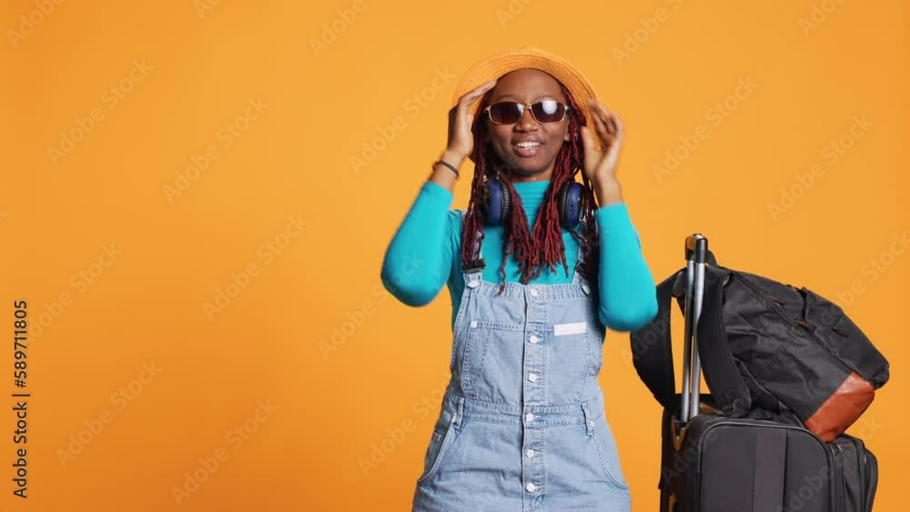 Excited woman wearing sunglasses and hat, feeling confident travelling to holiday destination. Young adult with luggage and trolley bags leaving on urban adventure, cool glasses. Excited woman wearing sunglasses and hat, feeling confident travelling to holiday destination. Young adult with luggage and trolley bags leaving on urban adventure, cool glasses.