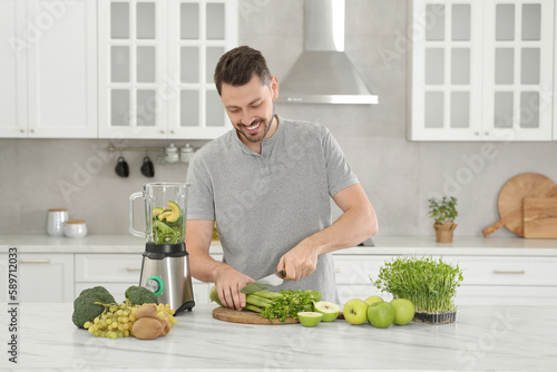 Happy man cutting celery for delicious smoothie at white marble table in kitchen © New Africa