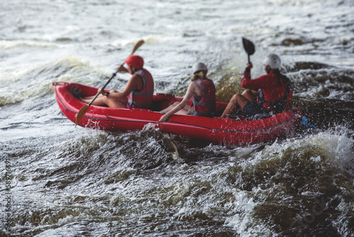 Raft boat during whitewater rafting extreme water sports on water rapids, kayaking and canoeing on the river, water sports team with a big splash of water, 3 persons in a raft boat