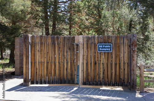 A dumpster enclosure with wooden doors and no public dumping sign.