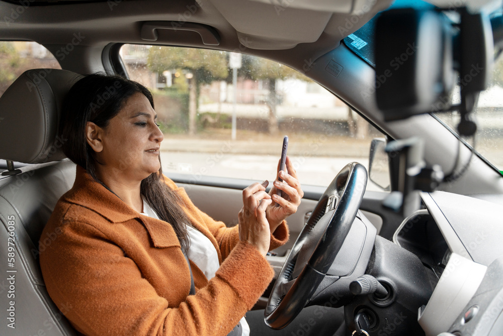 Portrait of busy mature Indian woman holding mobile phone driving car. Transportation, distracted driving concept