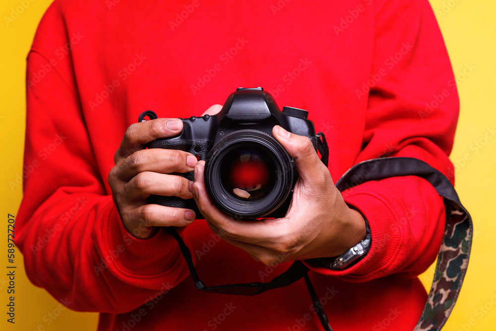 Man photographer in red shirt makes photos. Male hands hold the camera close-up and adjust lens. Digital single-lens reflex camera in hands. Man photographer in red shirt makes photos. Male hands hold the camera close-up and adjust lens. Digital single-lens reflex camera in hands.