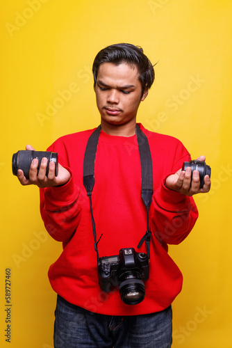 Quadro em tela Young Asian man in casual style with dslr camera confuse to choice lens against yellow background
