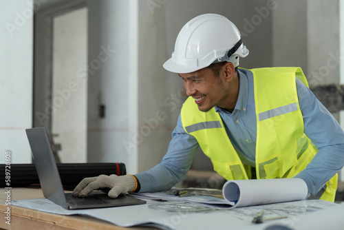 asian male engineer working with drawings inspection on laptop on construction site at work desk in office