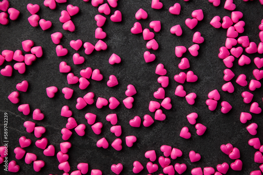 Pink heart sugar sprinkles scattered on dark Pink heart sugar sprinkles scattered on dark