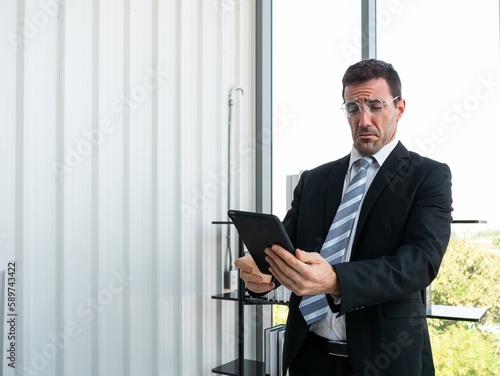 Caucasian businessman reading and looking farsighted on the tablet screen about marketing solution planing at the office company