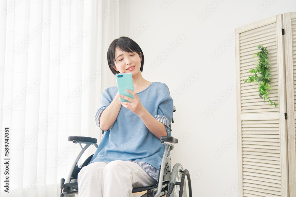 リビングでスマホを使う車椅子に乗った女性 リビングでスマホを使う車椅子に乗った女性