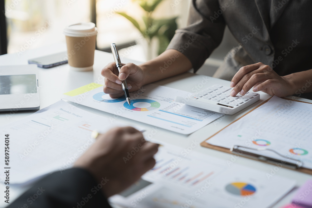 Team of business people is calculating with a calculator and discussing to record company financial growth statistics using graphs. The chart is a reference for auditing and analyzing the summary. Team of business people is calculating with a calculator and discussing to record company financial growth statistics using graphs. The chart is a reference for auditing and analyzing the summary.