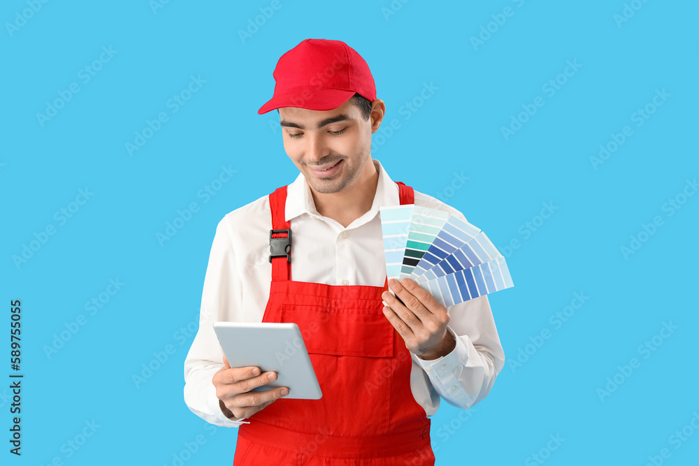 Male painter with color palettes and tablet computer on blue background Male painter with color palettes and tablet computer on blue background
