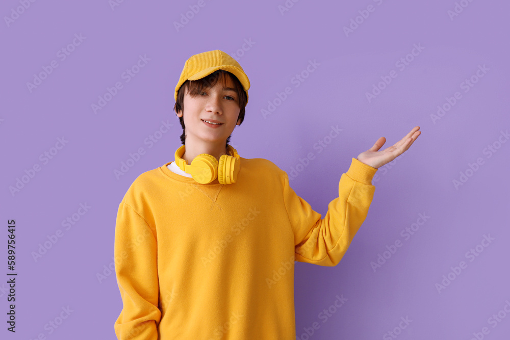 Teenage boy in cap with headphones showing something on lilac background