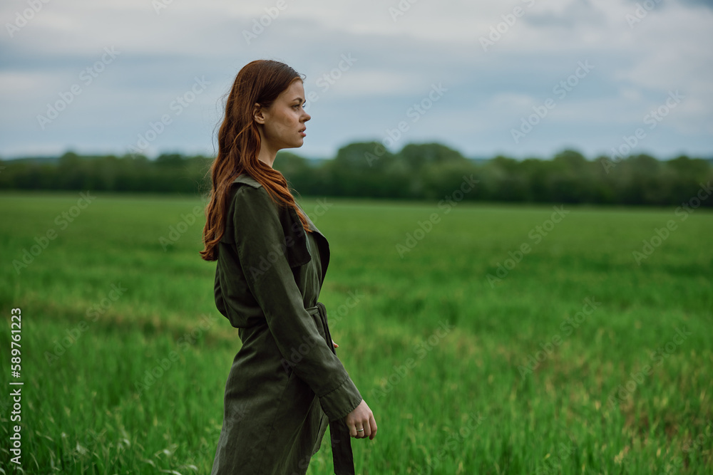 a beautiful, red-haired girl in a raincoat stands in a field in the spring in rainy weather a beautiful, red-haired girl in a raincoat stands in a field in the spring in rainy weather