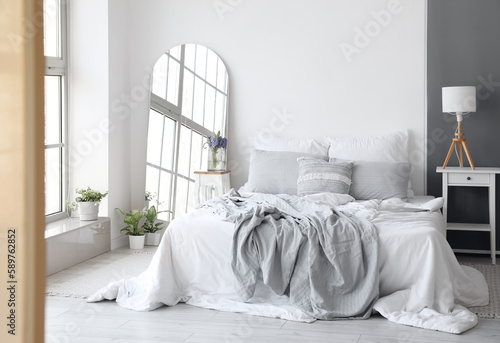 Interior of light bedroom with mirror and spring flowers in vase
