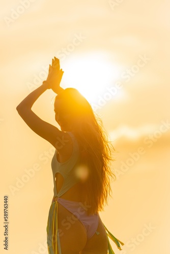 Back view of a beautiful caucasian sexy woman in bikini swimsuit by the beach with superb sunset and sun rays shinning across the sea