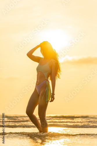 Beautiful caucasian sexy woman in bikini swimsuit by the beach with superb sunset and sun rays shinning across the sea