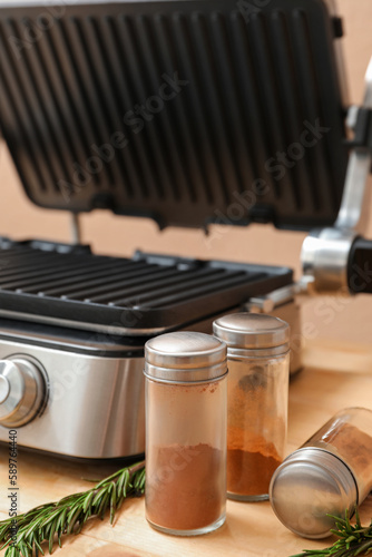 Modern electric grill with open lid  spices and rosemary on wooden table  closeup