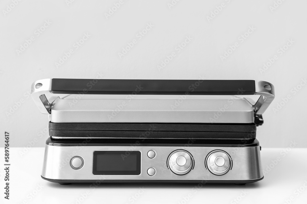 Modern electric grill with closed lid on white table against grey background Modern electric grill with closed lid on white table against grey background