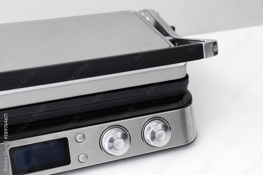 Modern electric grill with closed lid on white table, closeup Modern electric grill with closed lid on white table, closeup