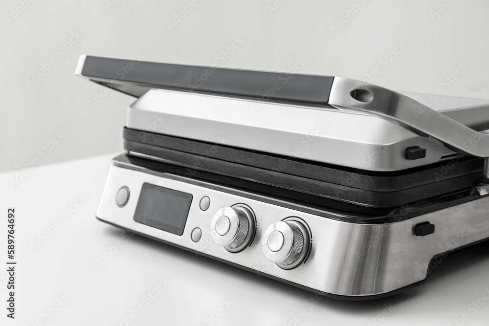 Modern electric grill with closed lid on white table against grey background, closeup Modern electric grill with closed lid on white table against grey background, closeup
