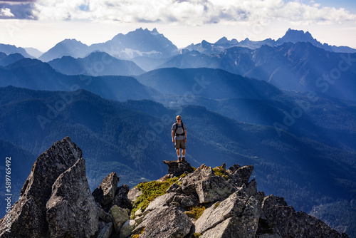 Adventurous athletic male hiker standing on top of a rugged mountain in the Pacific Northwest with jagged mountains in the background.  © Pelo Blanco Photo