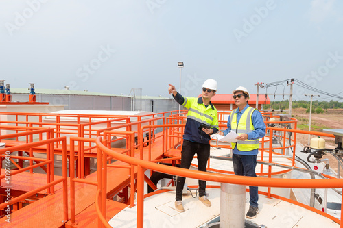 Two heavy industrial engineers standing in a standard water treatment plant use digital tablet computers and chatting. Asian industry professionals