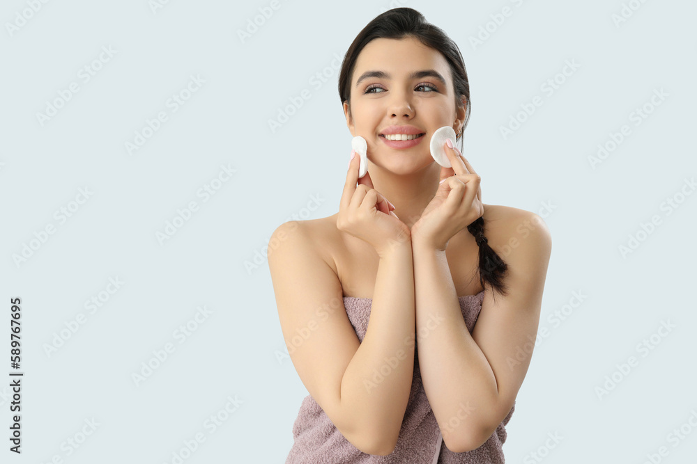 Young woman removing makeup with cotton pads on light background Young woman removing makeup with cotton pads on light background