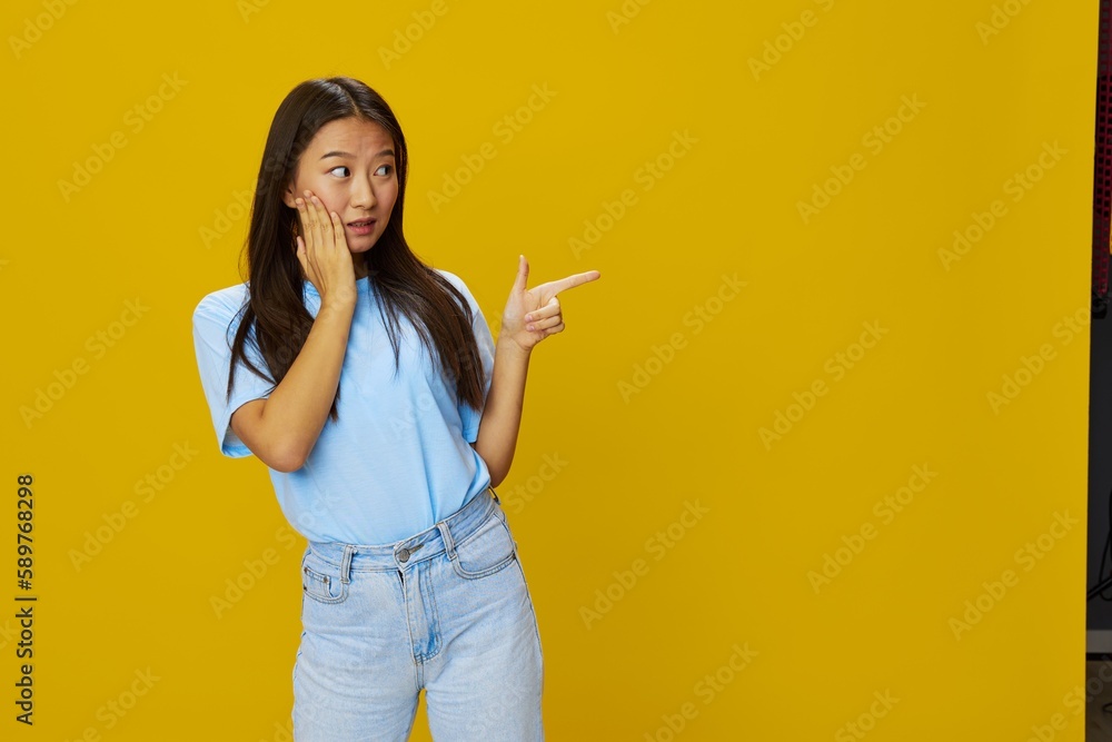 Asian woman smile with teeth hand gestures, signs and symbols on yellow background in blue t-shirt and jeans Asian woman smile with teeth hand gestures, signs and symbols on yellow background in blue t-shirt and jeans