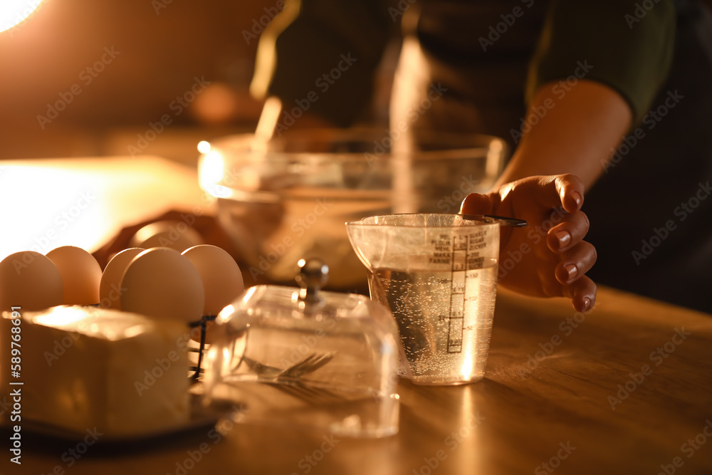 Woman making dough for pasta at table in dark kitchen, closeup