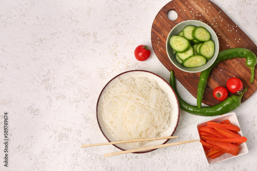 Composition with bowl of tasty rice noodles, chopsticks and vegetables on white grunge table