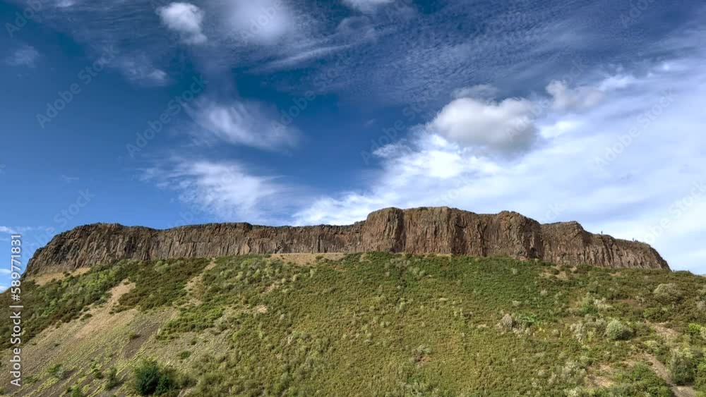 Big volcanic cliff, Salisbury Crags, Edinburgh, Scotland. Sunny summer sky top. City centre nature deforested grassy park view from below. Day Big volcanic cliff, Salisbury Crags, Edinburgh, Scotland. Sunny summer sky top. City centre nature deforested grassy park view from below. Day