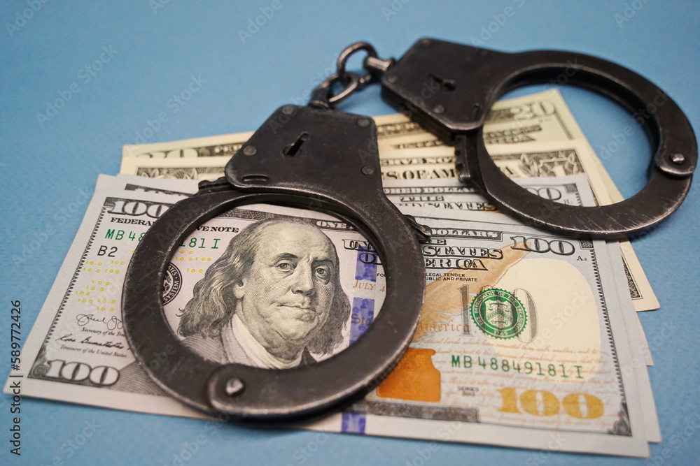 Almaty, Kazakhstan - 04.06.2023 : The handcuffs are on the hundred-dollar bills on the table. Almaty, Kazakhstan - 04.06.2023 : The handcuffs are on the hundred-dollar bills on the table.