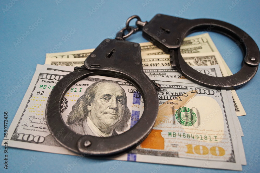 Almaty, Kazakhstan - 04.06.2023 : The handcuffs are on the hundred-dollar bills on the table. Almaty, Kazakhstan - 04.06.2023 : The handcuffs are on the hundred-dollar bills on the table.