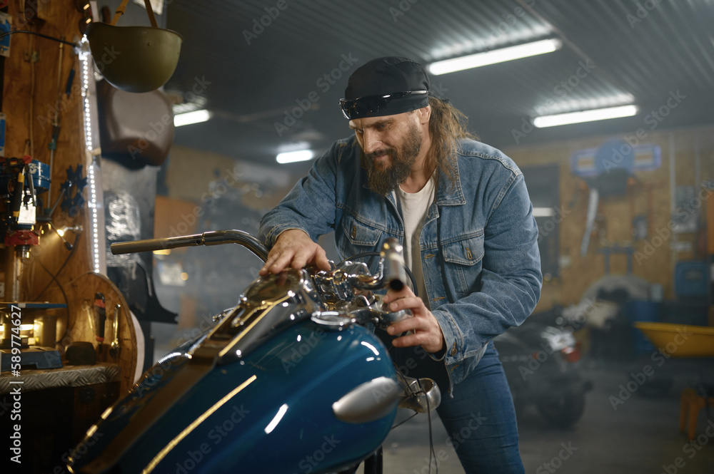 Mature male biker examining his new motorbike standing with garage