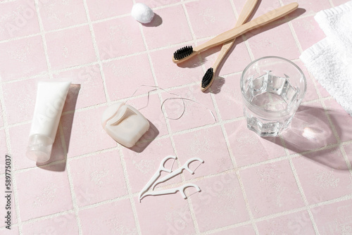 Dental floss, toothpicks, brushes, toothpaste and glass of water on pink tile table