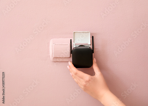 Woman plugging black WiFi repeater in electric socket on pink wall photo